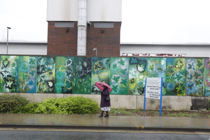 Joyce Baptise standing by the section of mural she helped to paint outside Newham General Hospital
