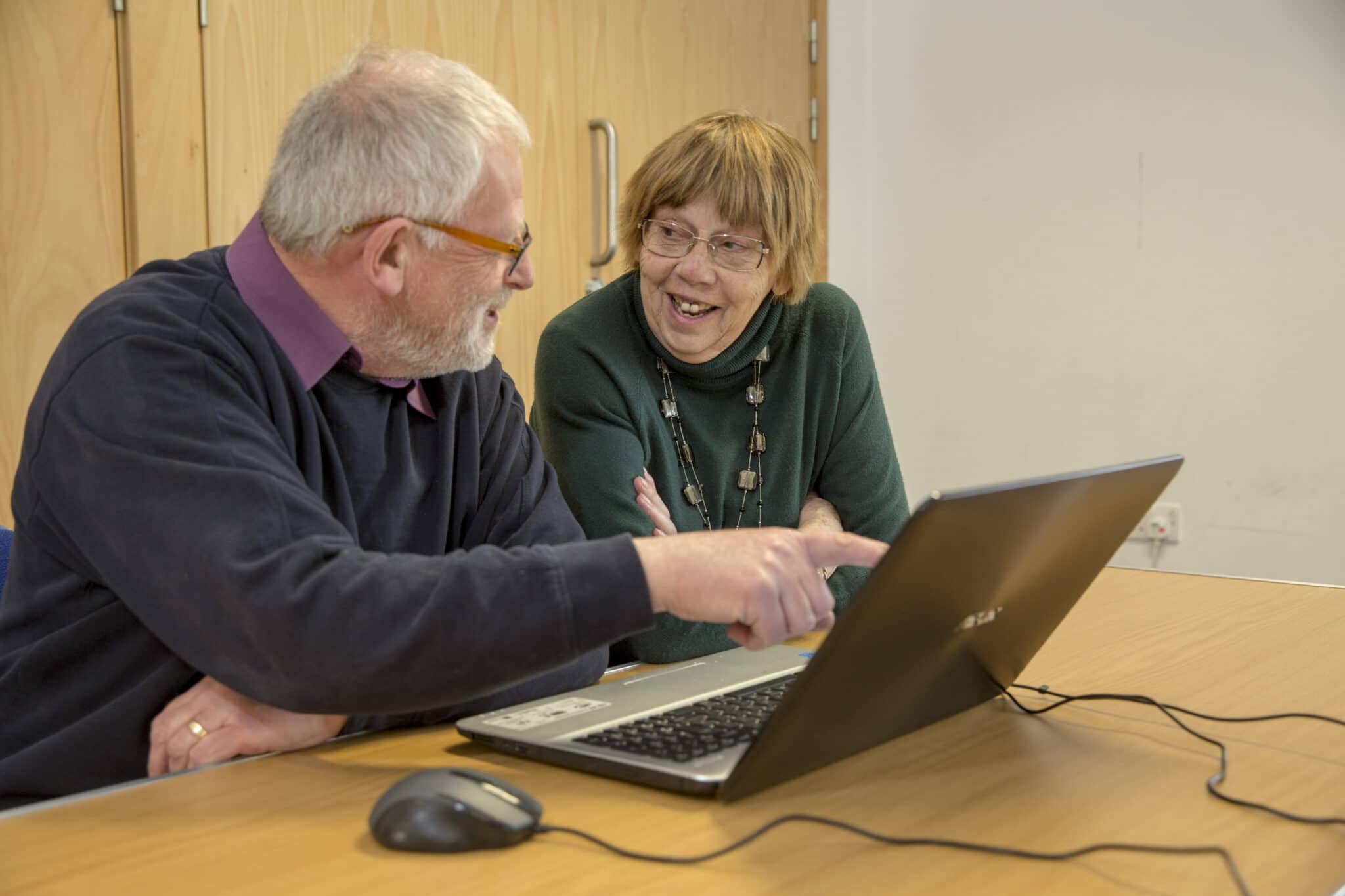 Two people at a laptop, pointing and smiling