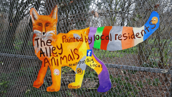 A hand painted fox on a fence with the words 'The Alley Animals painted by local residents'