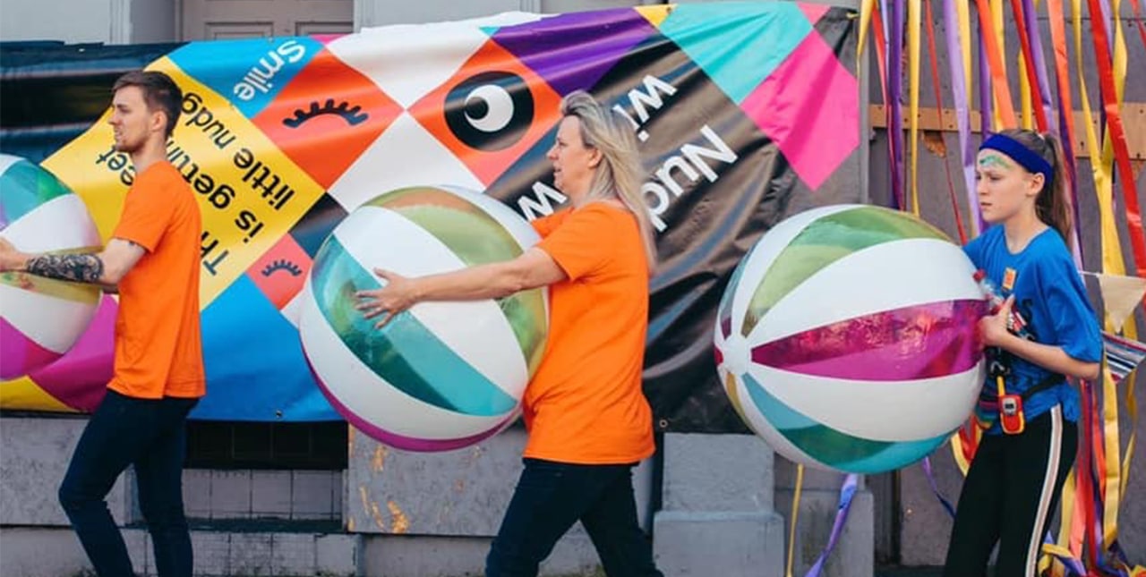 Three people carrying large beachballs down the street