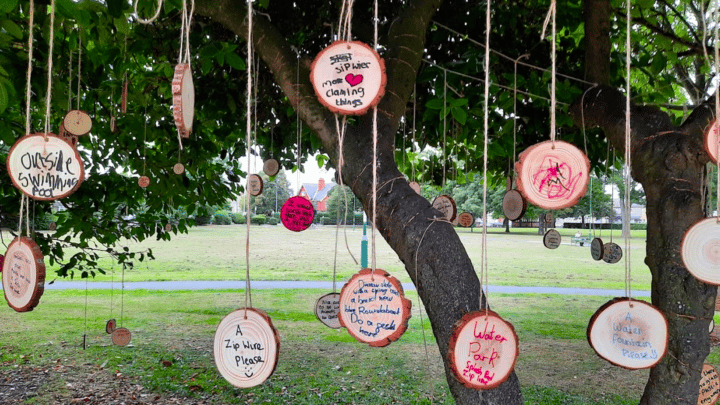 A tree that has wooden coasters with written requests from the community hanging off the branches