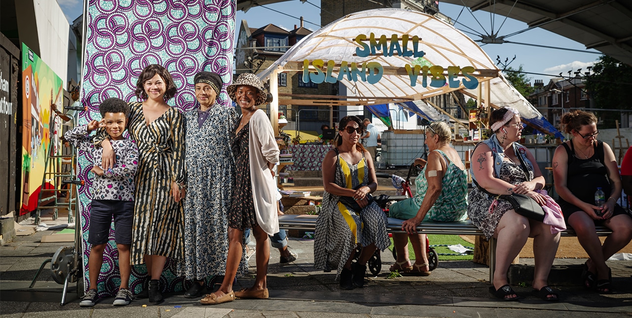 A group standing in front of a patterned backdrop on the left, and another talking in front of a stage on the right