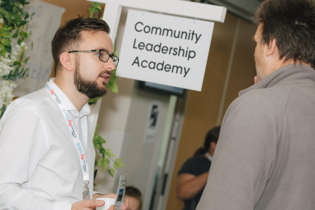 Two people speaking with 'Community Leadership Academy' sign in the background