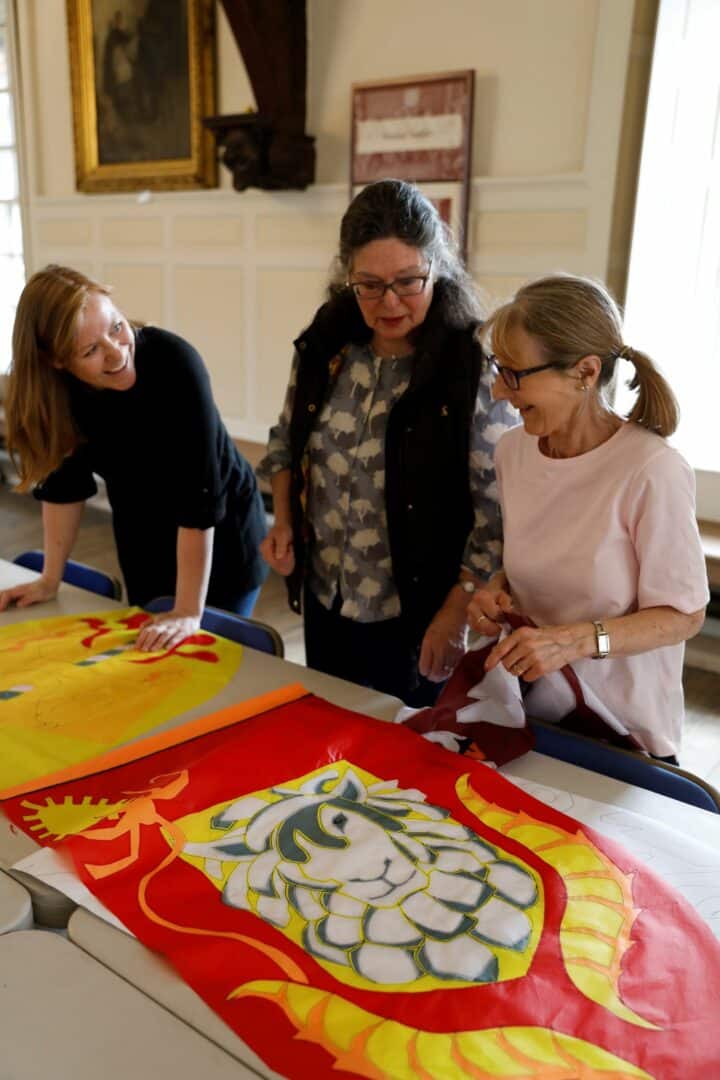 Women look at a tapestry on a table