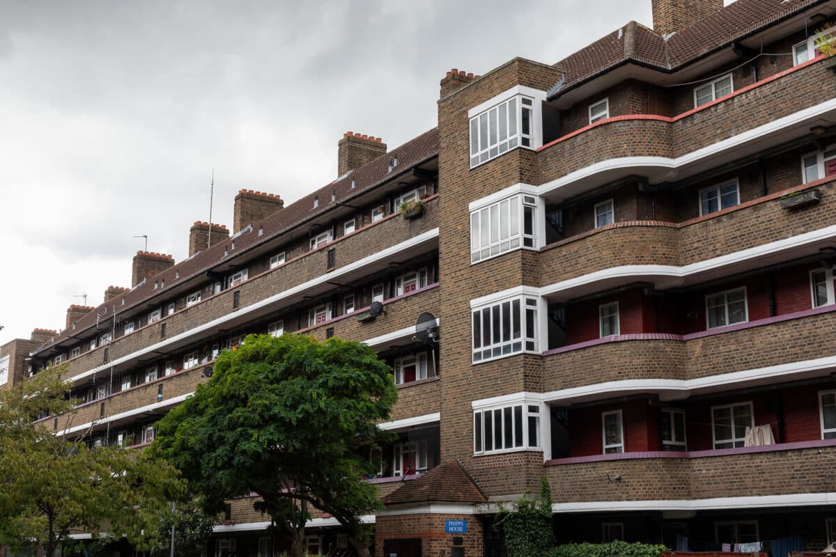 Five storey block of red brick flats. Trees with green leaves are planted in front.