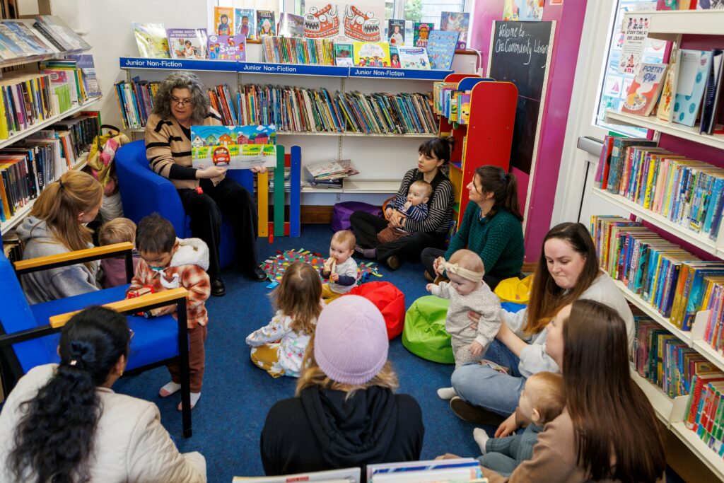 A volunteer shows a story book to a group of children and their mums in Ore community library