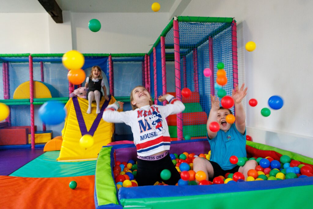 Three children play on slide and ball pit in a sensory soft play centre