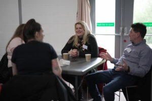 Three people sit around a table chatting and smiling