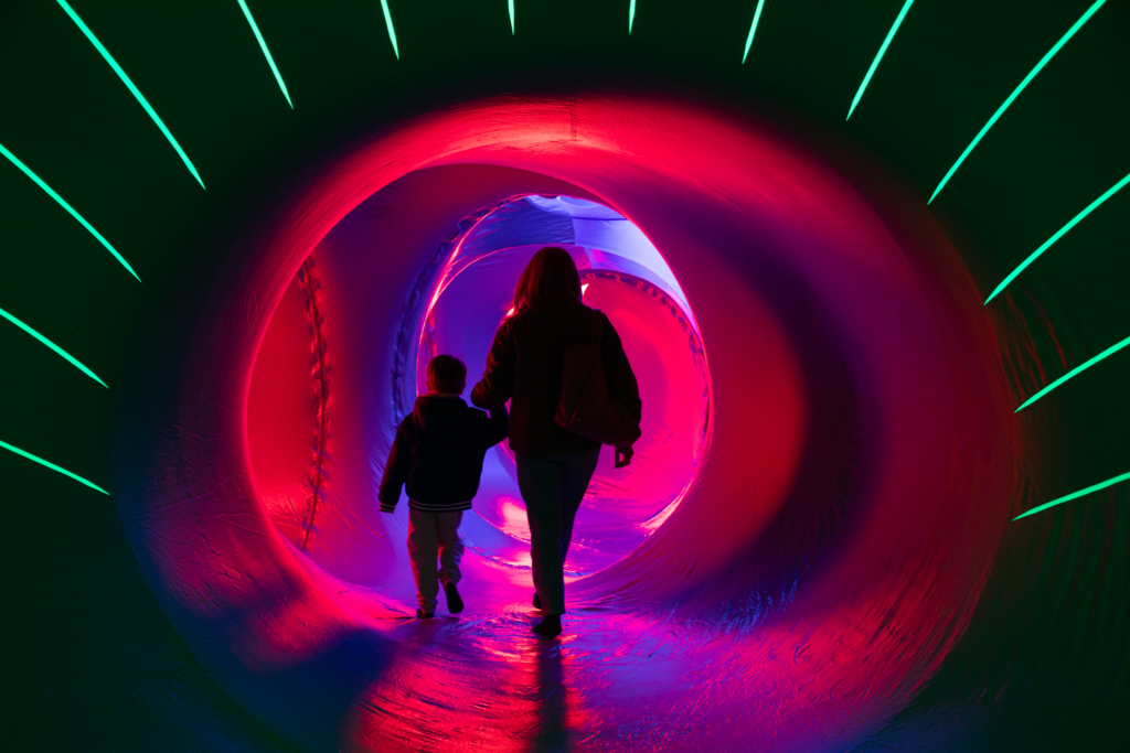 Two people walk through lit up inflatable tunnel