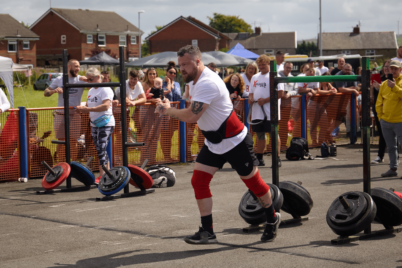 Man runs forward as he takes part in strong man competition in front of a mixed crowd of people