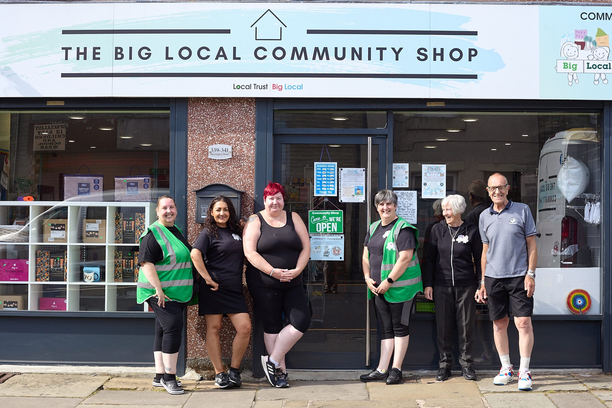 Six people stand outside a shop with a sign that reads 'The Big Local Community Shop'