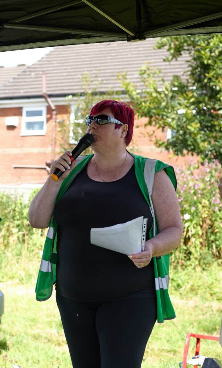 Elaine wearing a green high vis jacket and speaking into a microphone