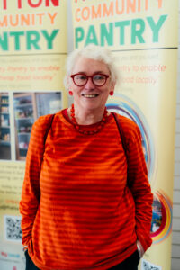 Anna Potten smiles while standing in front of two Fratton Together banners wearing a bright orange top