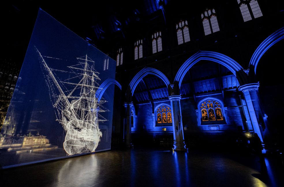 A white light installation of a ship is projected inside a blue-lit Victorian church