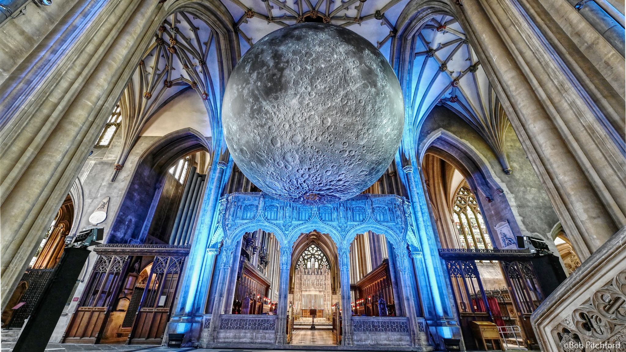 A huge art installation where a moon surrounded by light appears to float from the ceiling of a Victorian church