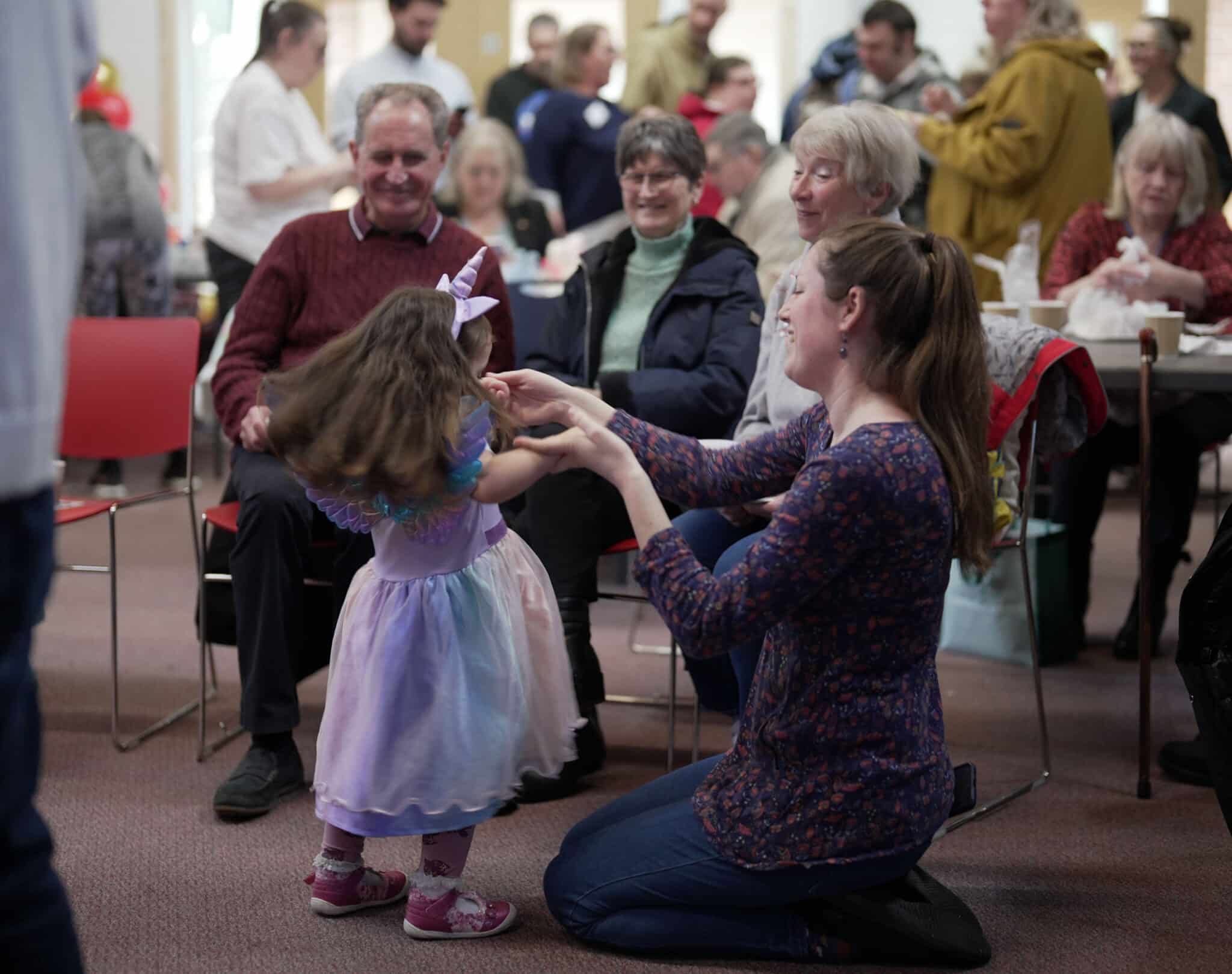 Group of people smile looking at little girl twirling in a purple dress