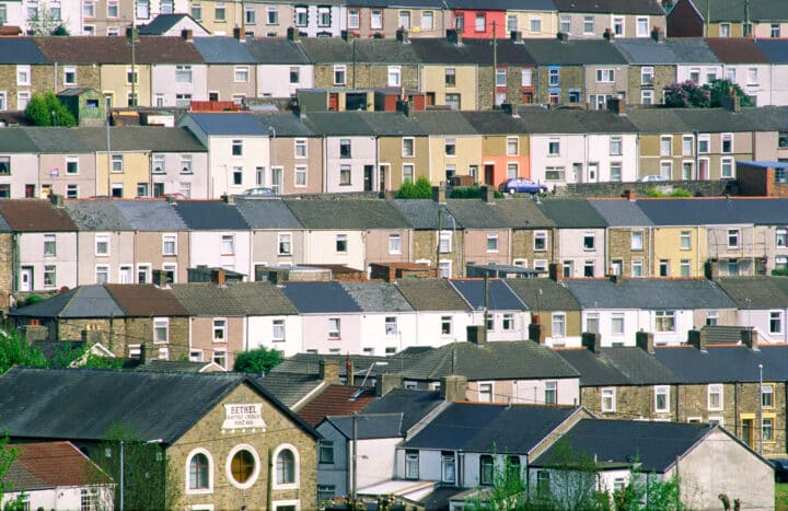 A hillside neighborhood with rows of terraced houses. The houses have similar architectural styles but the colours of the houses vary, with some painted in pastel shades and others in natural brick tones.