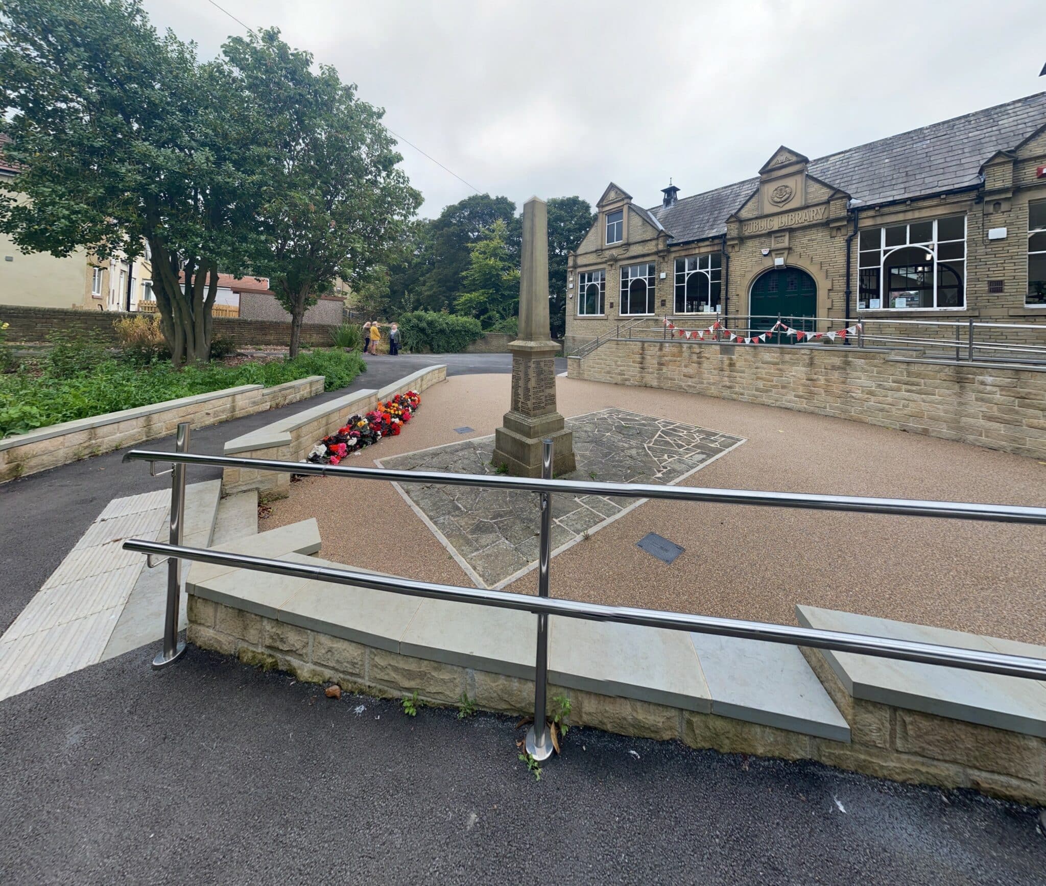 A ramp with a metal handrail leads down to a brick community library building.