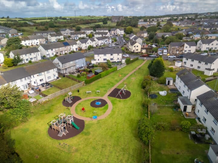 An aerial view of a children's park with an array of play equipment set in a green grassy area. Surrounding the park are terraced houses.
