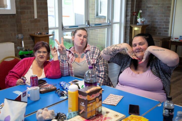 Three ladies sitting by a table posing for the camera