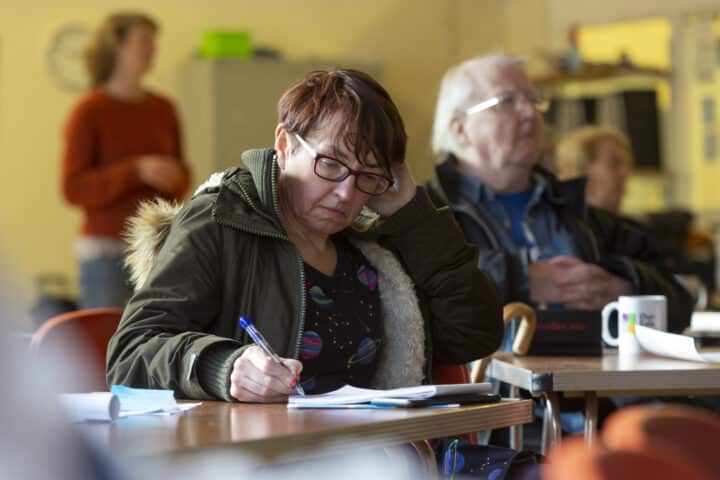 Woman writing notes at a local community meeting with other residents