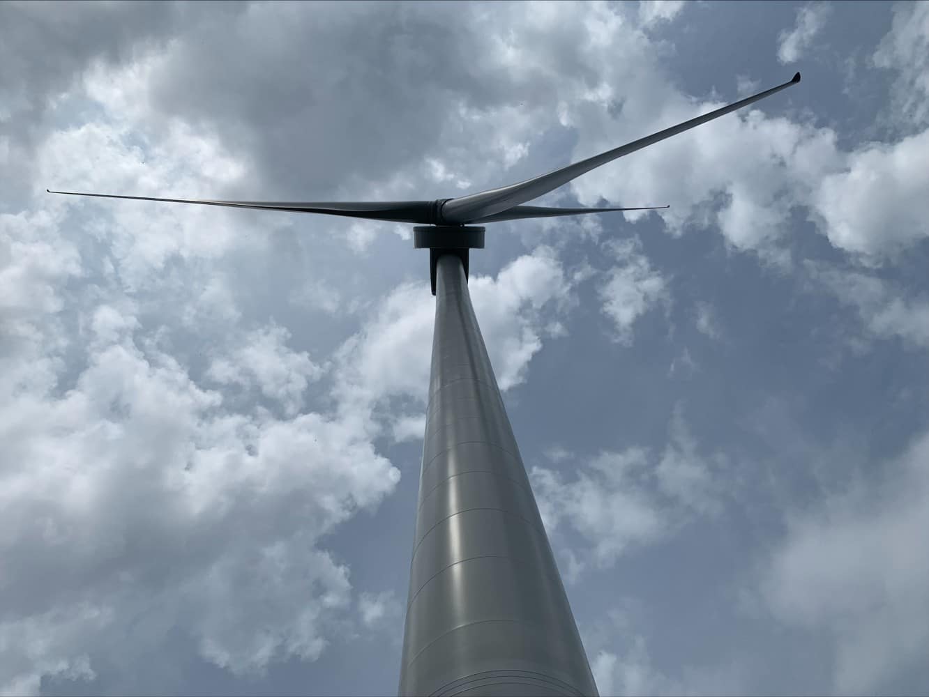 A wind turbine with its blades spanning a cloudy blue sky.